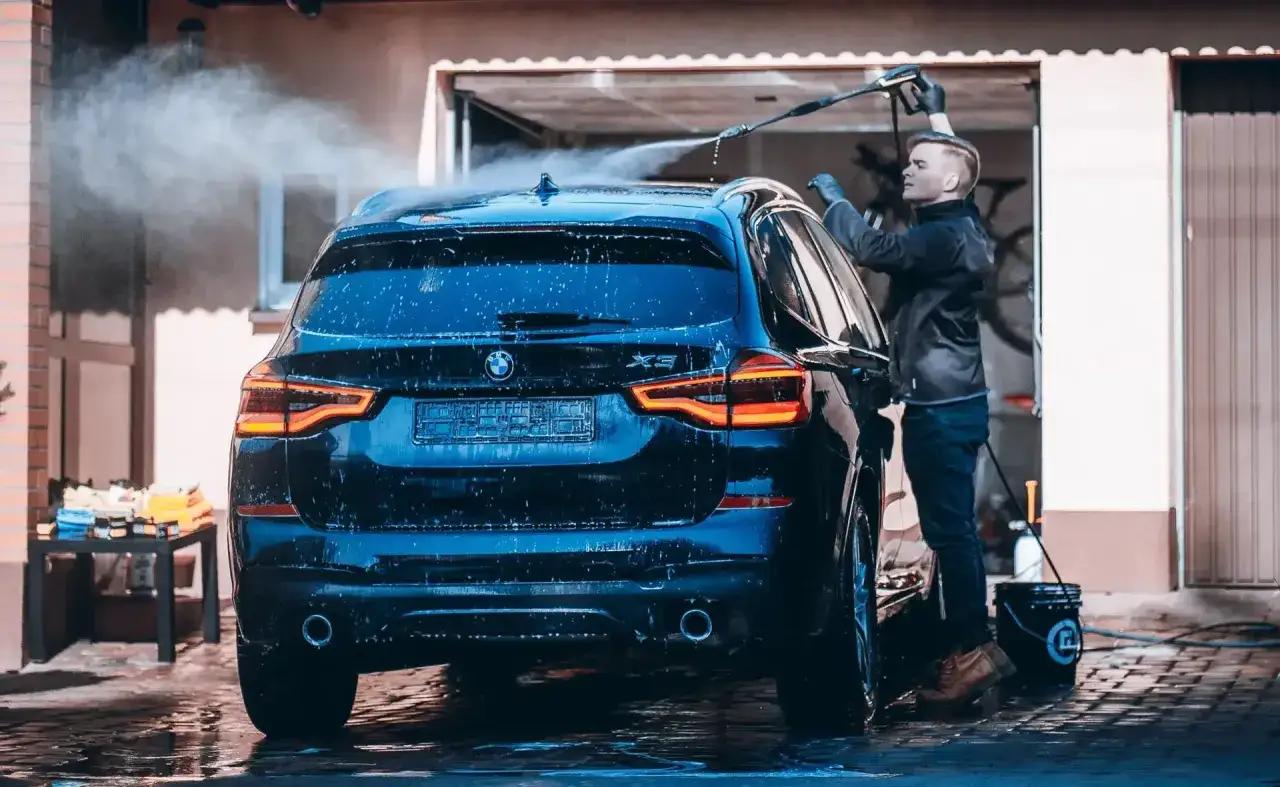Młody mężczyzna myje czarne BMW pod domem. Woda spływa po karoserii. Czy można myć auto w zimie? Tak, jeśli zadbasz o odpowiednie warunki.