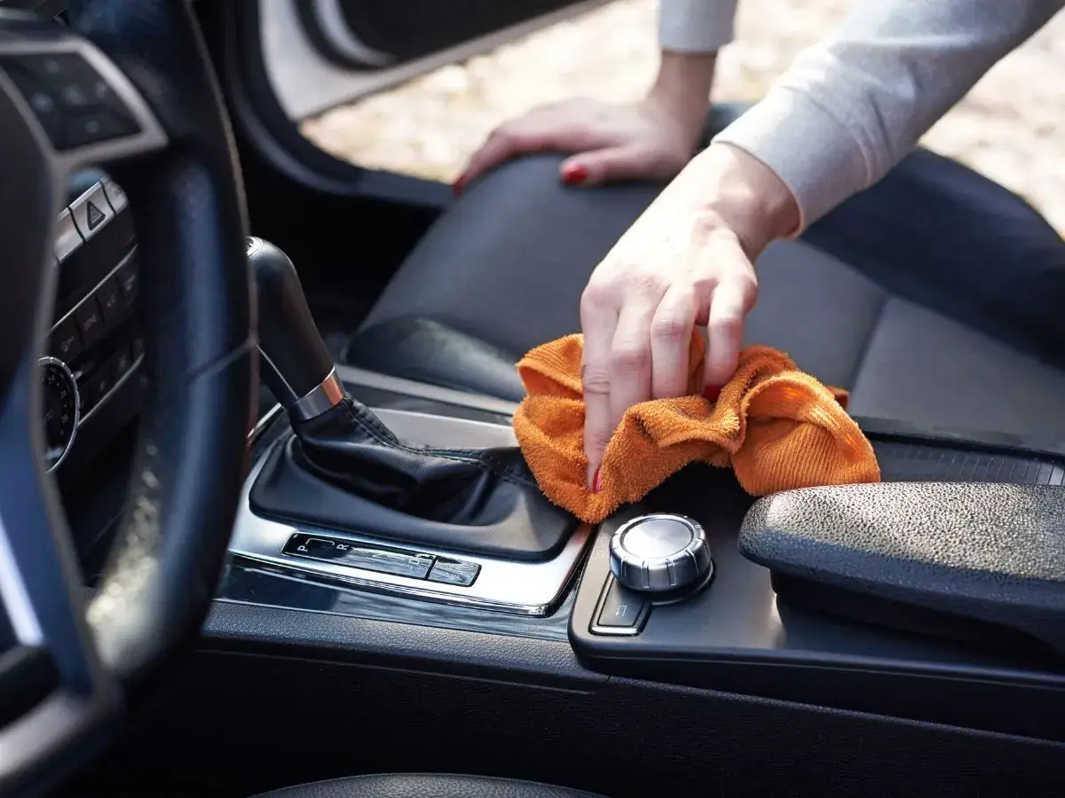 Dłoń z pomarańczową ściereczką czyści konsolę środkową luksusowego samochodu, element profesjonalnego auto detailing.