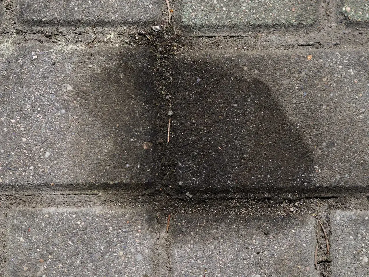 Stare plamy z oleju silnikowego na kostce brukowej. Ciemna, rozlana plama na szarym podłożu.