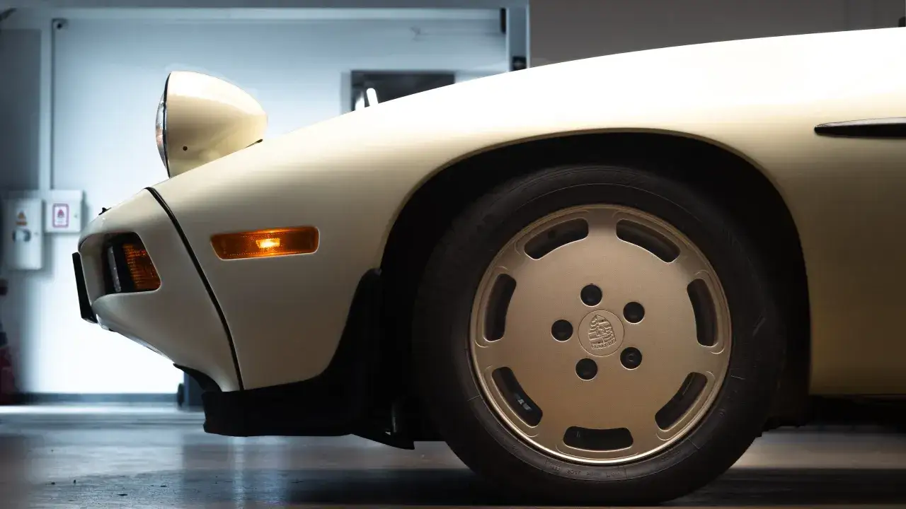 Klasyczny Porsche 928 w studio detailingowym, z wysuniętymi światłami i złotą felgą.