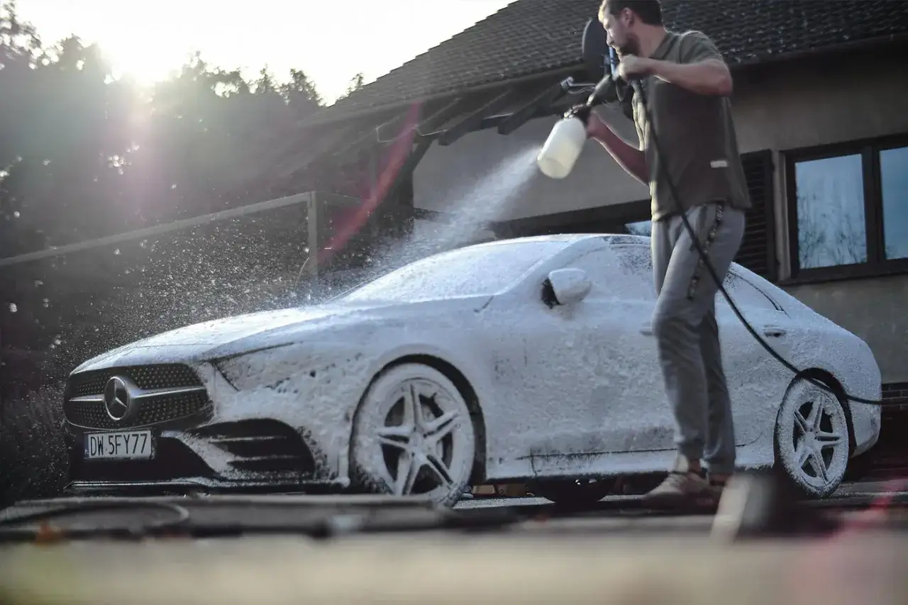 Mężczyzna wykonuje mycie detailingowe luksusowego Mercedesa, pokrywając go obfitą pianą.