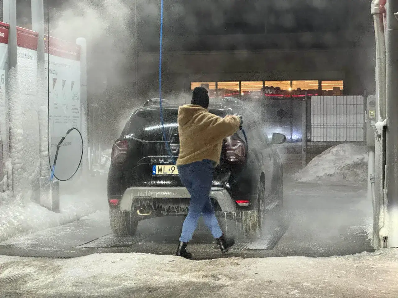Ktoś myje auto zimą na myjni bezdotykowej. Wok&oacute;ł śnieg i l&oacute;d, a z myjki leci piana.