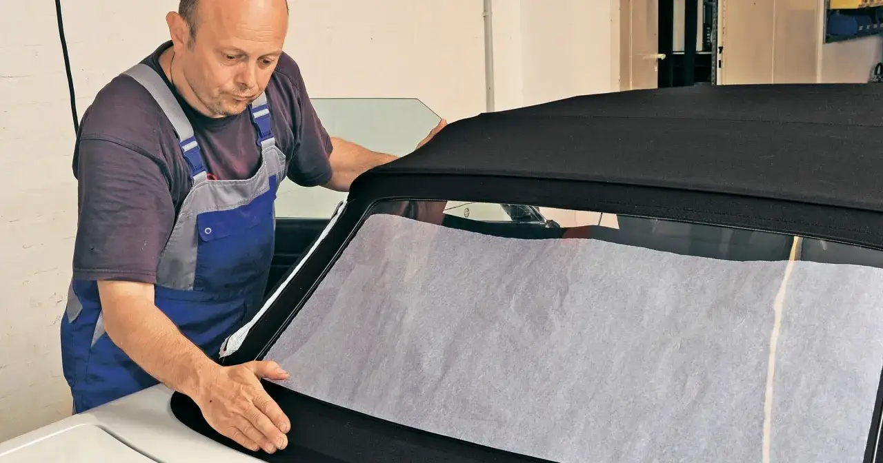 Mechanik w kombinezonie pracuje nad dachem cabrio, przygotowując go do szycia.