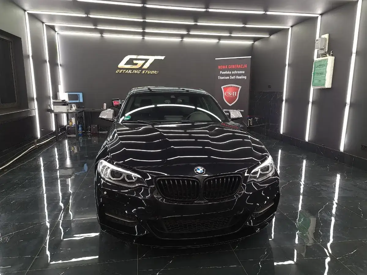 Lśniący czarny BMW w studiu detailingowym. W tle logo GT Detailing Studio i nowoczesne wyposażenie studia detailingowego.