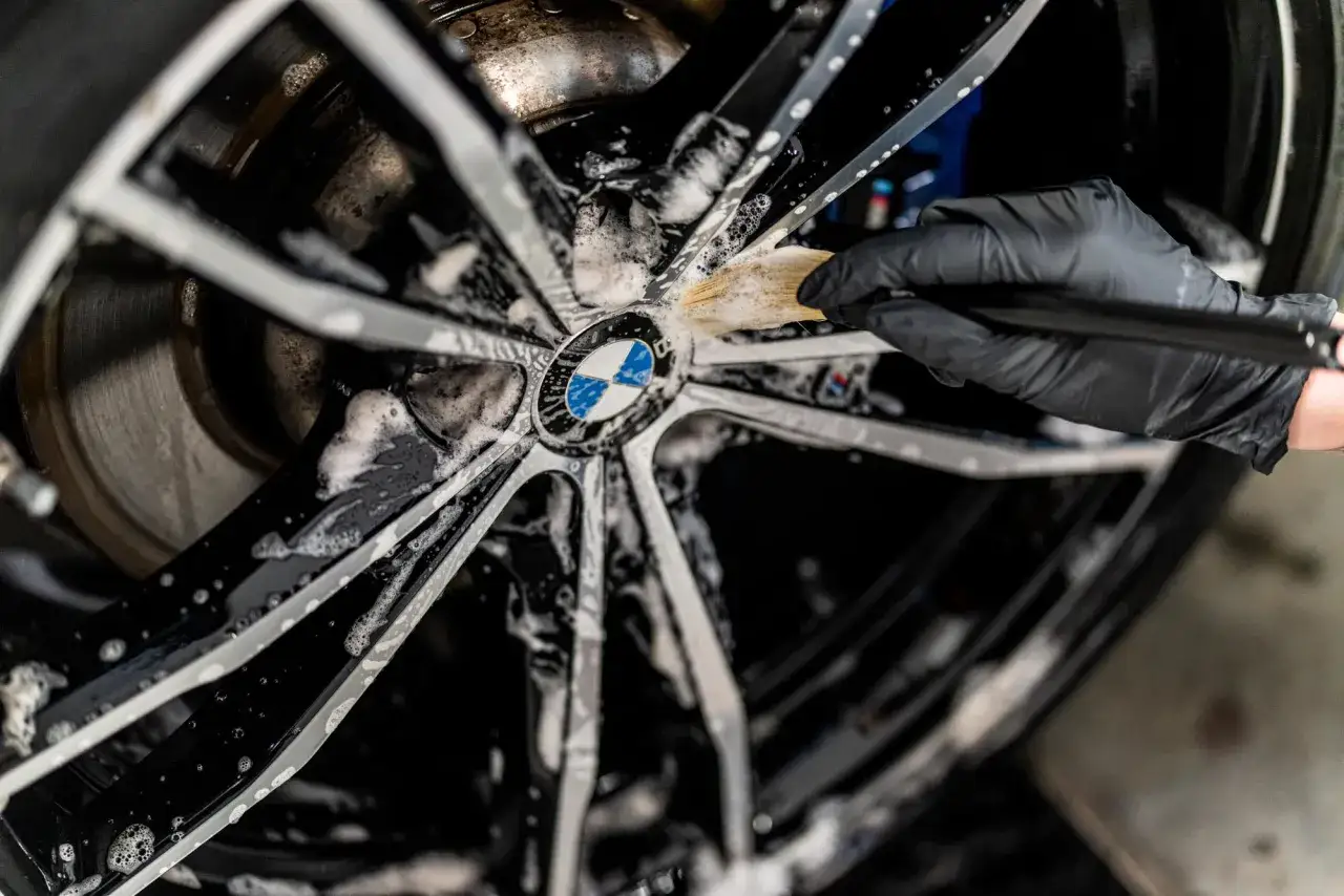 Rękawiczka w czarnej rękawiczce czyści felgę BMW, używając piany i pędzelka. Czyszczenie felg WD40 to klucz do lśniącego wyglądu.