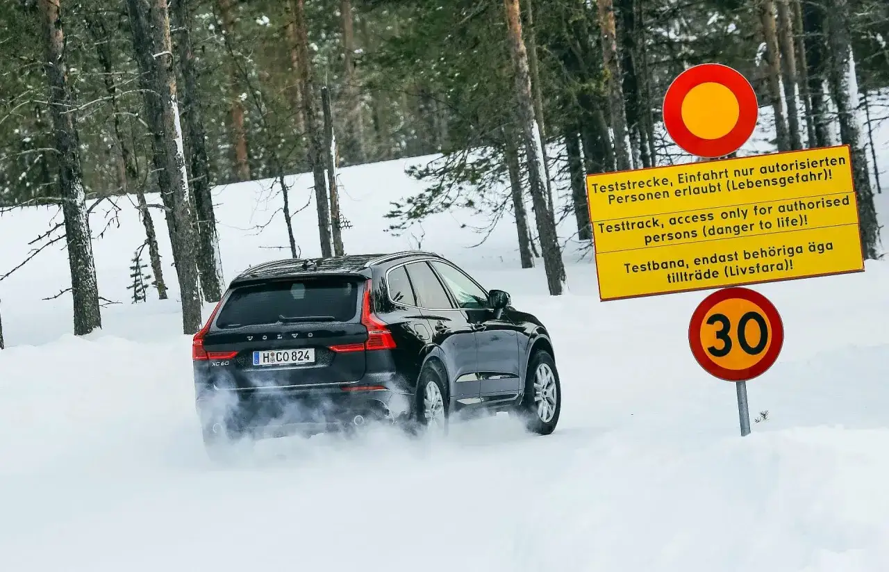 Czarny Volvo XC60 na śniegu, testujące dobór opon zimowych. Znaki ostrzegają o testowym torze i ograniczeniu prędkości do 30 km/h.