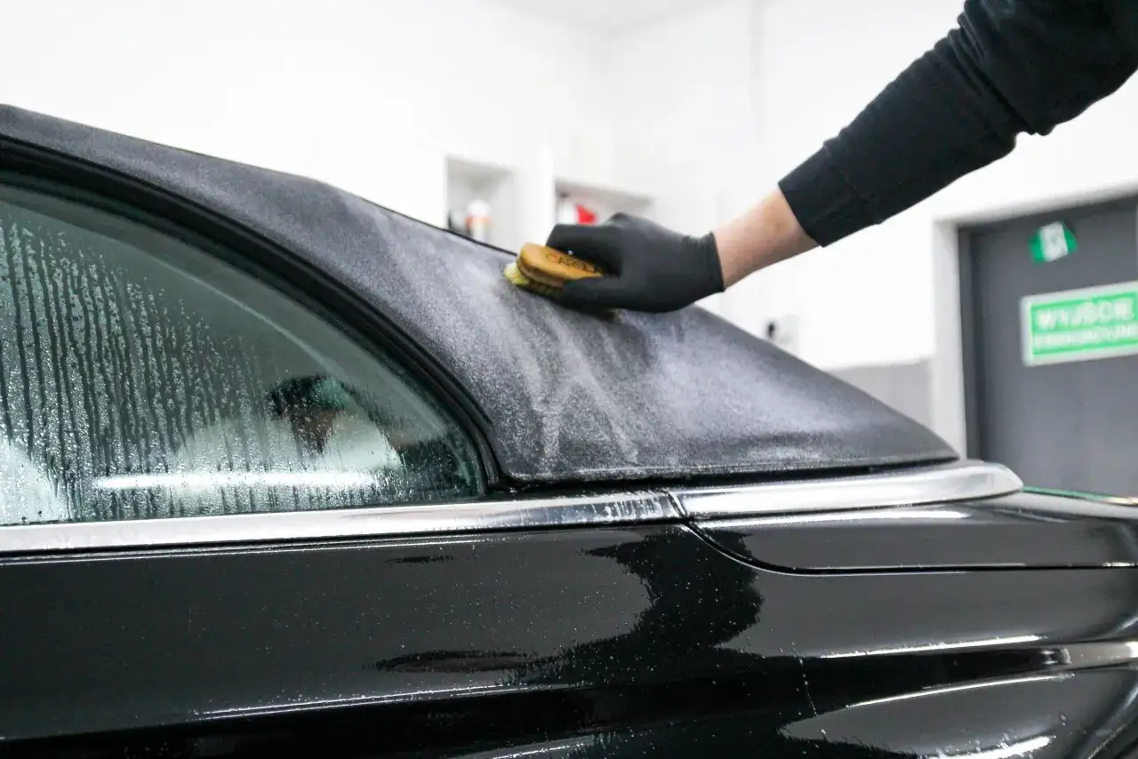 Rękawiczka w czarnej rękawicy delikatnie czyści dach cabrio, usuwając drobne zabrudzenia.