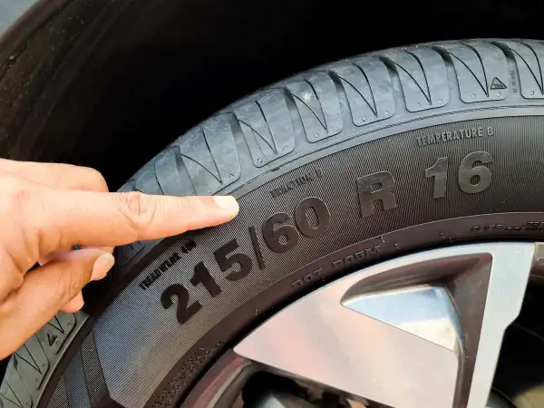 Palec wskazuje na oznaczenie opon 215/60 R16. Informacja ta jest kluczowa przy zakupie nowych opon.