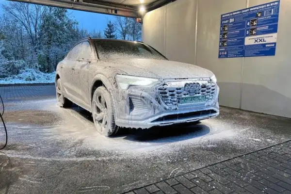 Audi pokryte pianą na myjni bezdotykowej zimą. Śnieg na drzewach w tle.