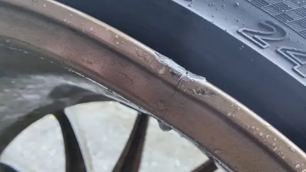 Pęknięta felga aluminiowa z widocznym uszkodzeniem i kroplami wody.
