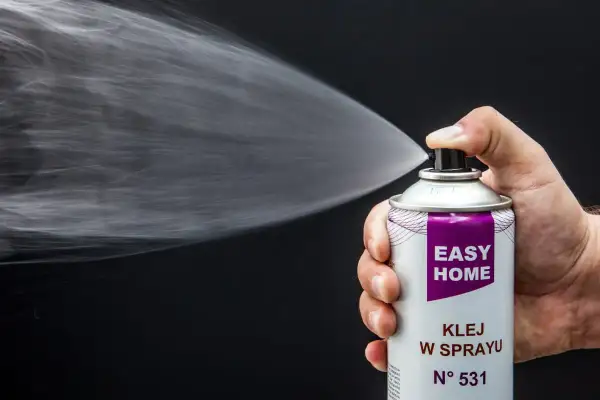 Dłoń trzyma puszkę z klejem w sprayu, który jest idealny, by przykleić podsufitkę w samochodzie.