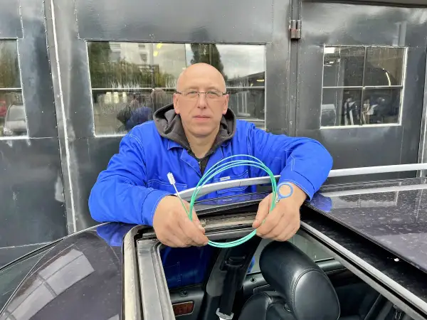 Mechanik z Audi A6 C6 pokazuje, jak udrożnić odpływ wody z podszybia. Używa do tego zielonego wężyka i szczoteczki.