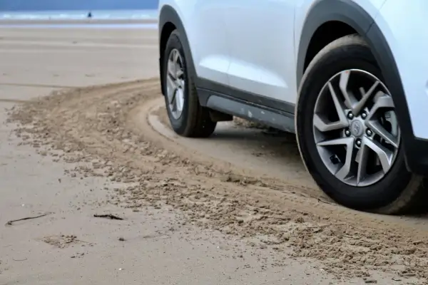 Białe auto na plaży, z widocznymi srebrnymi felgami. Zastanawiasz się, jaki kolor felg do białego auta będzie najlepszy? Te wyglądają świetnie!
